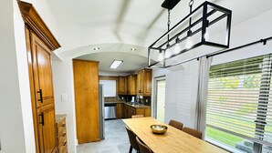 A modern kitchen with wooden cabinets, a stainless steel refrigerator, and a dining area with a long wooden table and chairs. - Beautiful 3 Bedroom 3 Bath Home w/ Pool Access (Fort Lauderdale)