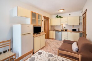 Cozinha compacta com geladeira, micro-ondas e fogão, área de refeições com mesa e cadeiras, e sala de estar com sofá.
