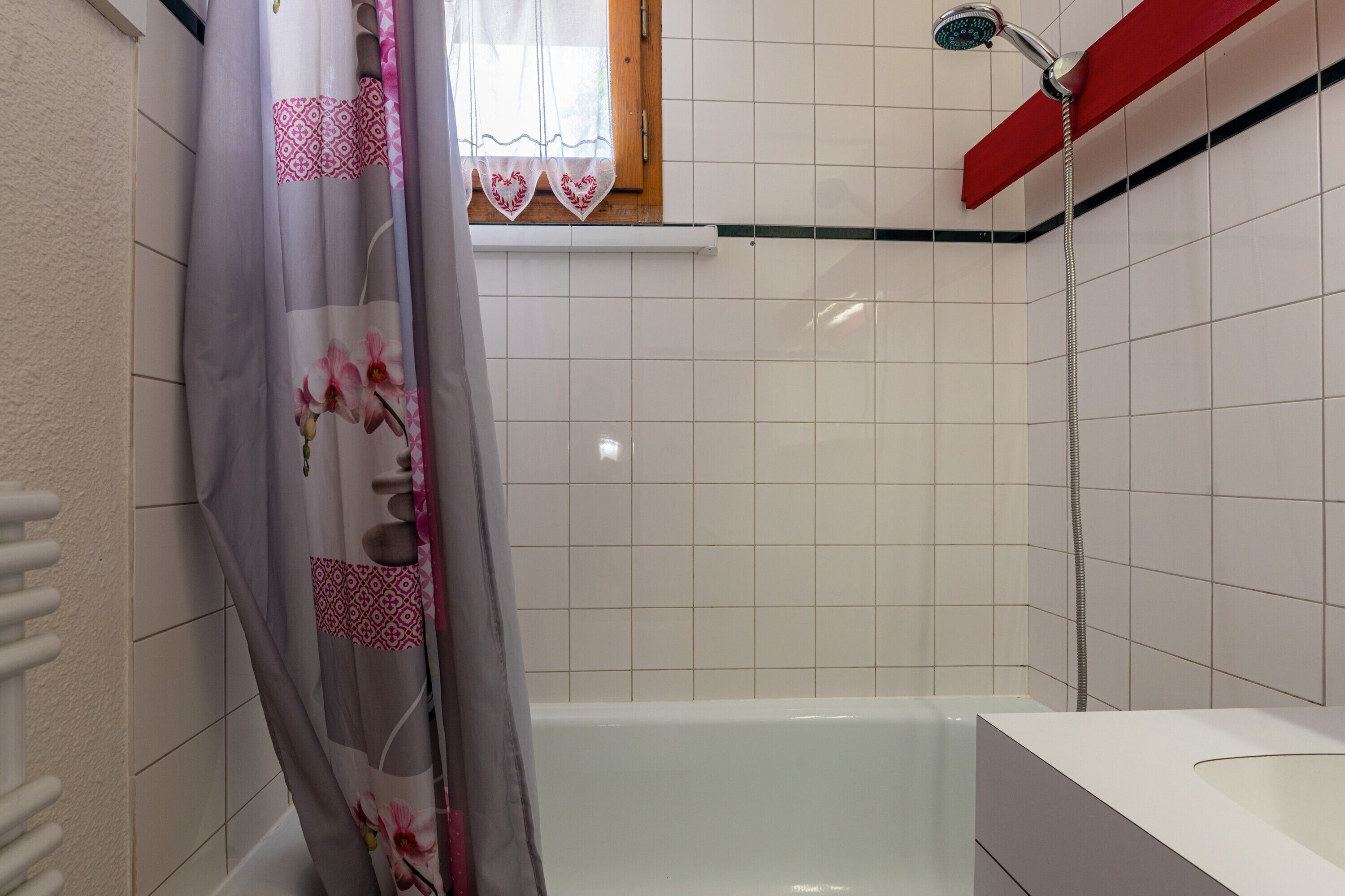 A bathroom with a bathtub, a showerhead, and a window with a curtain.