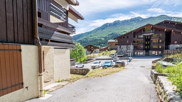 Eine Berghütte mit befestigter Auffahrt, geparkten Autos und Blick auf die Berge.