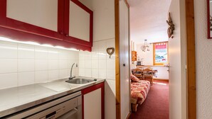 Eine Küche mit Spüle, Schränken und Geschirrspüler. Ein Flur führt zu einem Schlafzimmer mit Bett und Kommode.