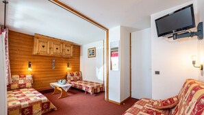 Ein gemütliches Zimmer mit Holzwänden, einem an der Wand befestigten Fernseher und einem Bett mit Decke.