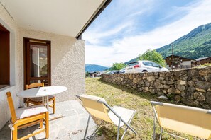 Un patio con mesa y sillas, un muro de piedra y vistas a coches y montañas.