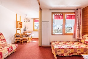 Una habitación acogedora con dos camas, una mesa de comedor, sillas, un radiador y una ventana con cortinas.