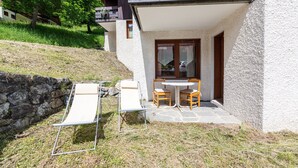 Eine Terrasse mit Tisch und Stühlen, einem Liegestuhl und einer Steinmauer.
