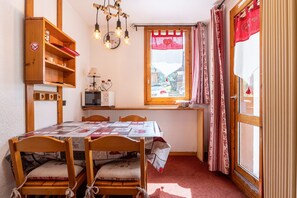 Un comedor con una mesa, sillas, un estante de madera, un reloj y una ventana con cortinas.