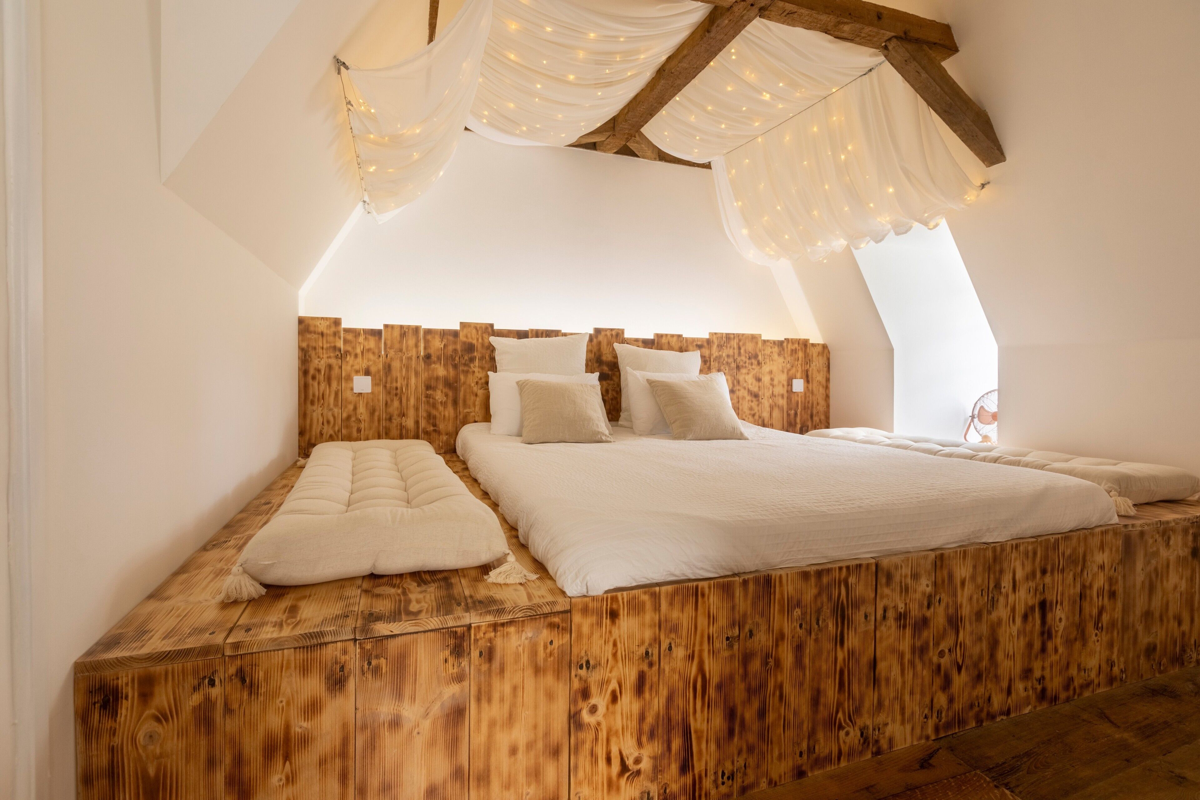 A bedroom with a wooden headboard, a large bed, and a sloped ceiling with draped fabric.