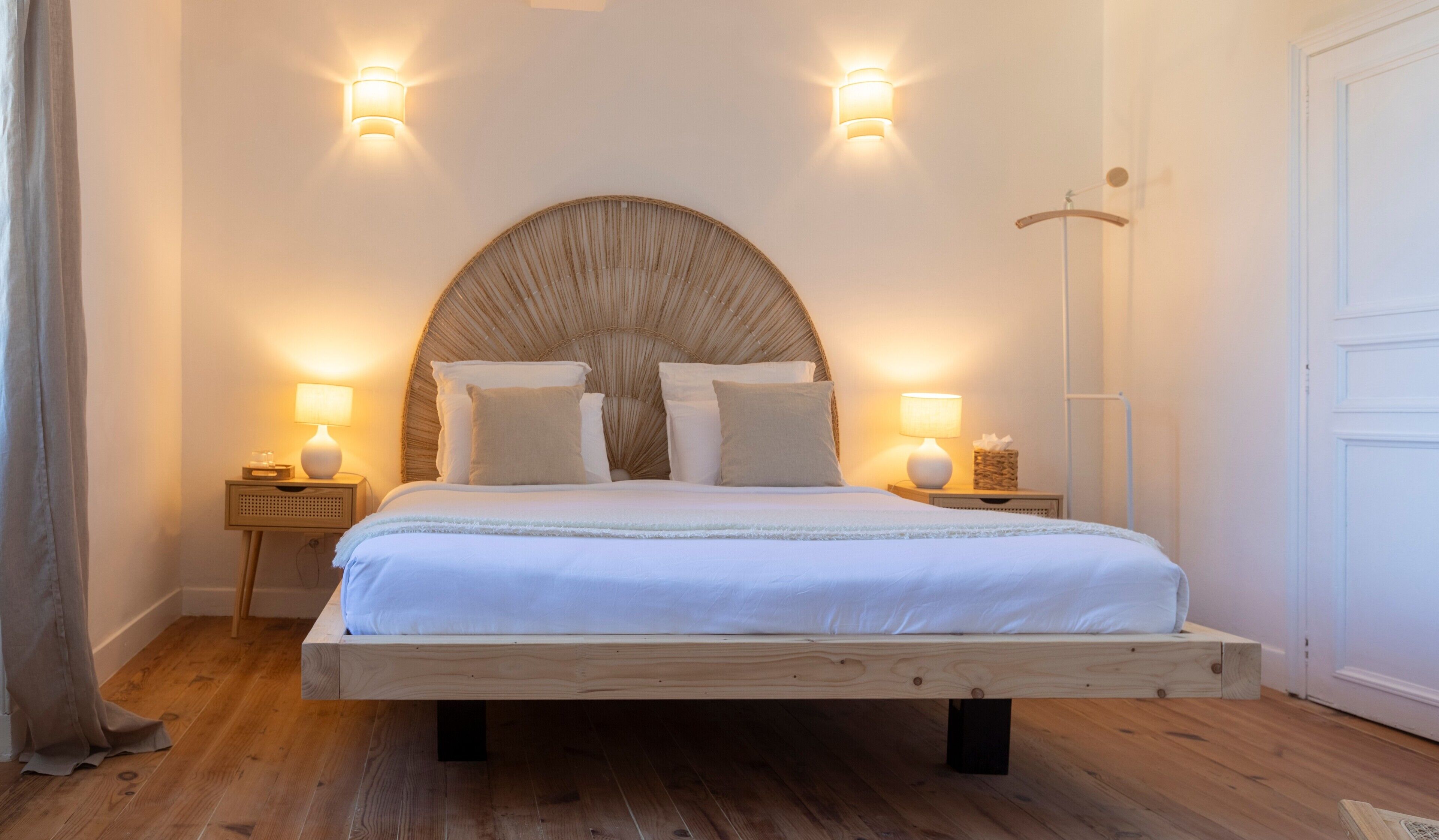 Ein Bett mit Holzrahmen, zwei Nachttische mit Lampen und ein großes, gewebtes Kopfteil.