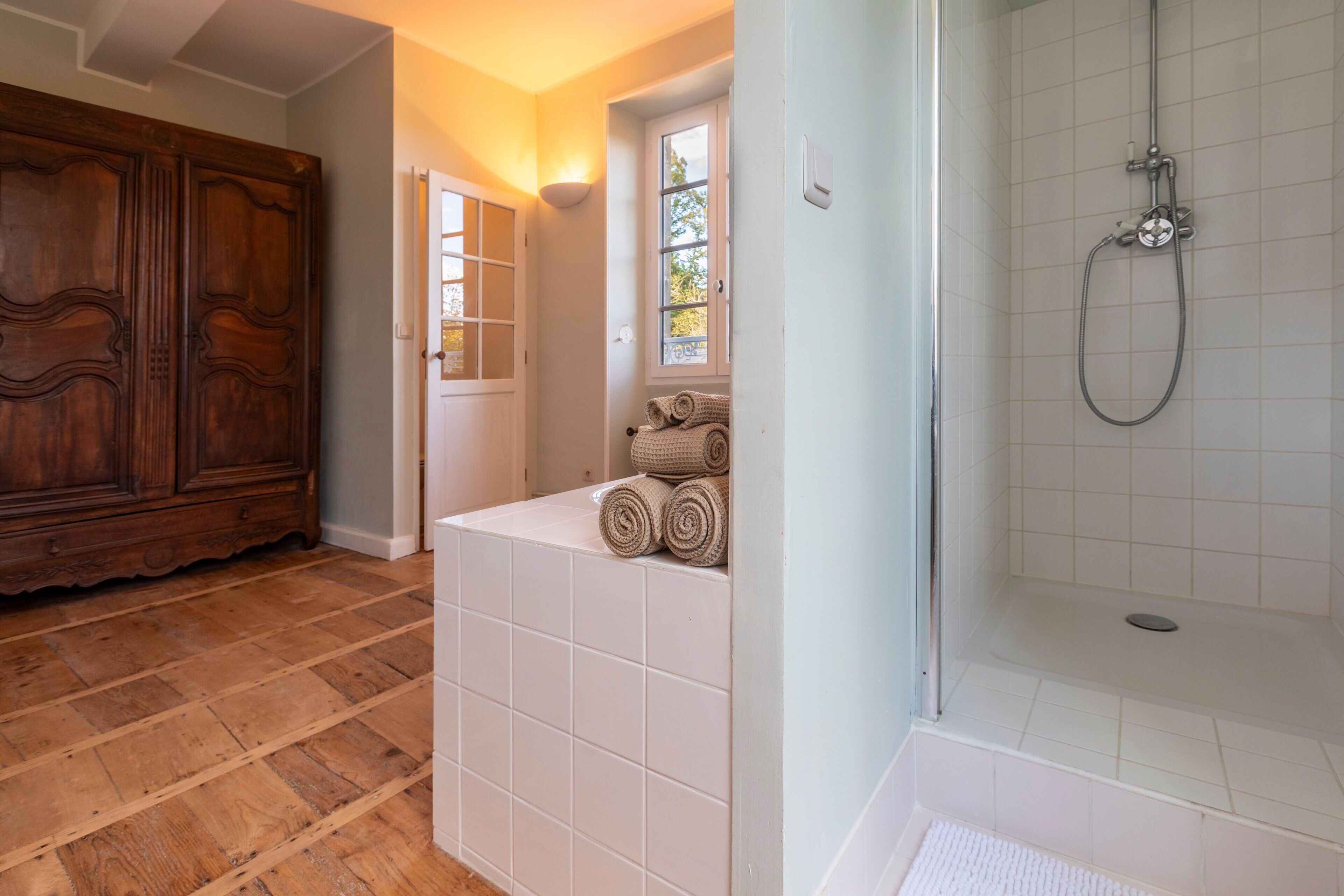 Een badkamer met een douche, een houten garderobe en een raam met uitzicht.