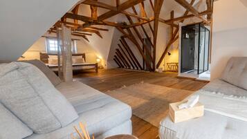 Slaapkamer in een loft met schuine plafonds, houten balken, een bed, een bank en een douchecabine met glazen wanden.