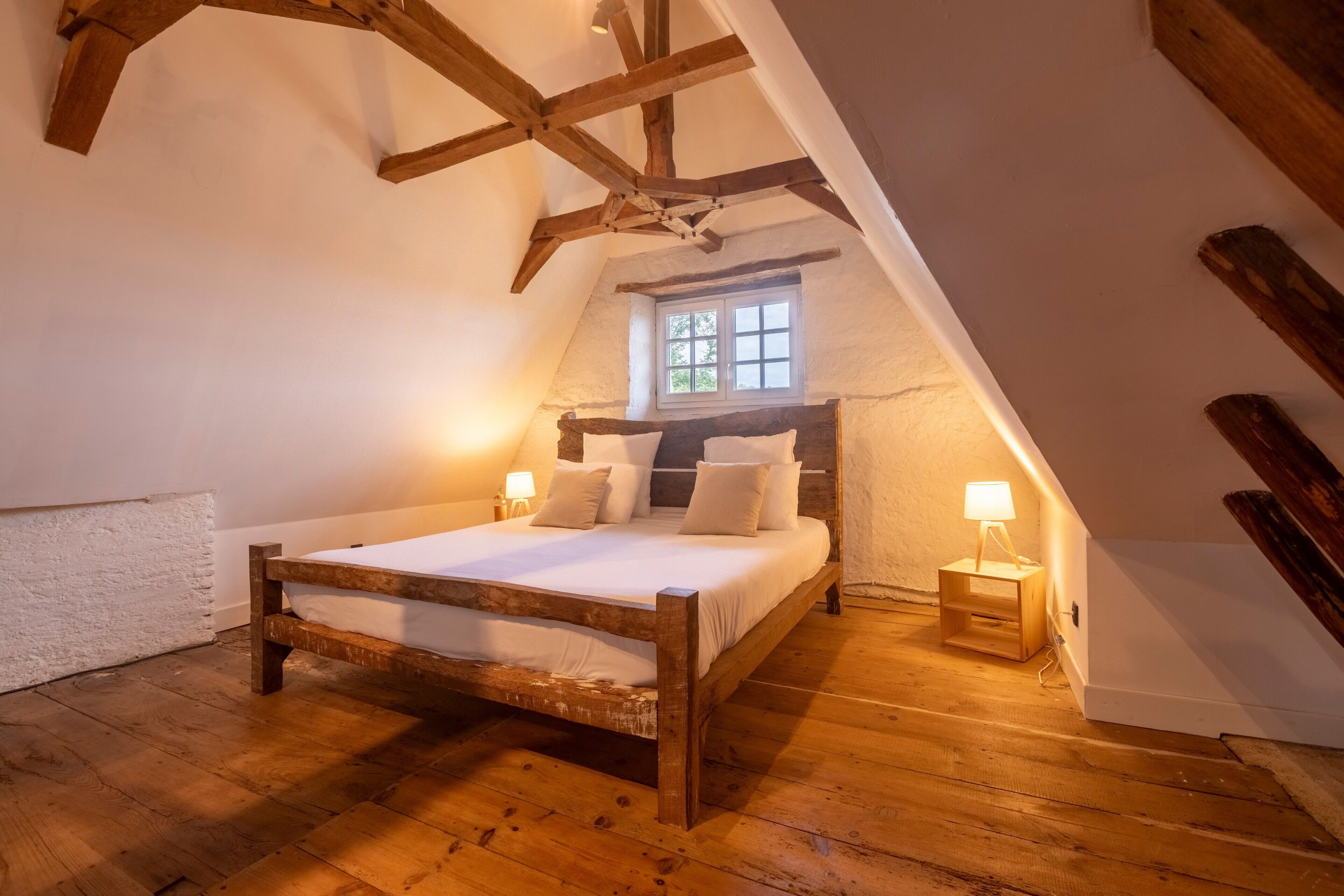Une chambre à coucher avec un lit en bois, une fenêtre et une table de chevet avec une lampe.