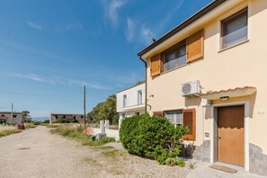 Un bâtiment à deux étages, avec une façade de couleur beige, une porte en bois et un petit jardin.