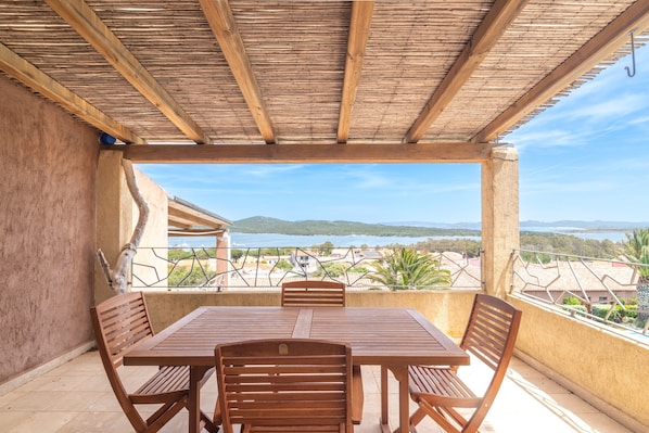 A covered outdoor seating area with a table and chairs, overlooking a scenic landscape.