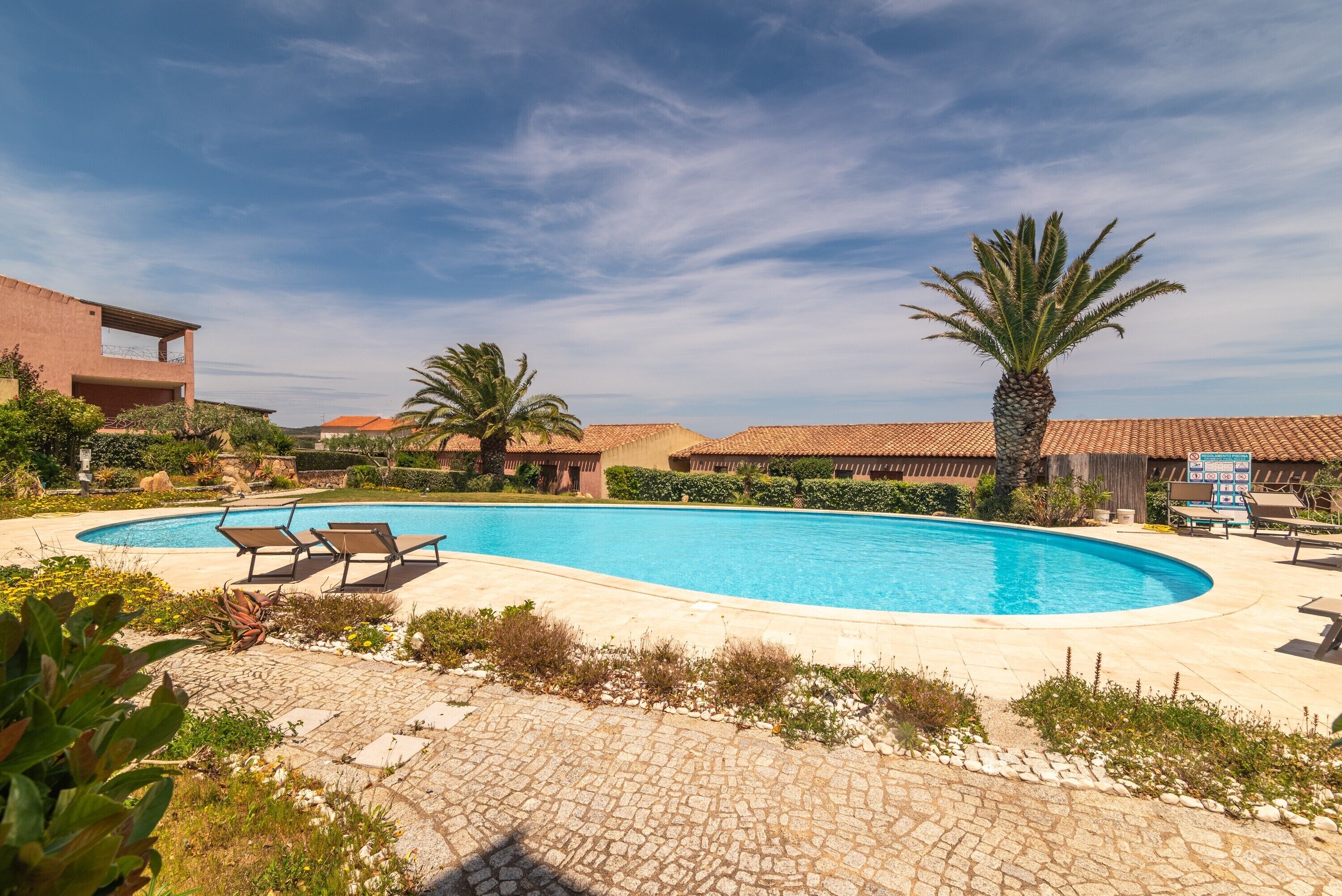 Ein Swimmingpool mit Liegestühlen, Palmen und blauem Himmel.