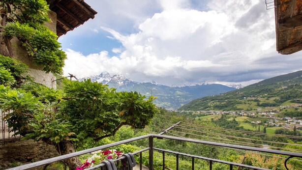 Een balkon met uitzicht op een bergachtig landschap, een stenen muur en een rustiek gebouw.