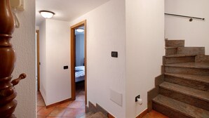 Een trap met een leuning, een deur die leidt naar een andere kamer, en een lamp aan de muur.