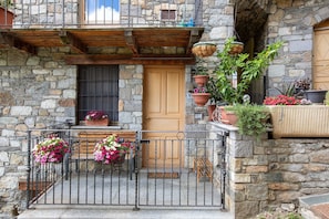 Un bâtiment en pierre avec une porte en bois, un balcon doté de rampes en métal et des plantes en pot.