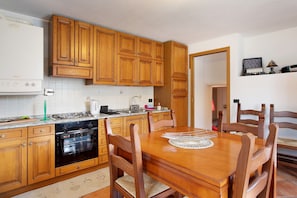 Une cuisine avec des meubles de rangement en bois, une cuisinière, un four et une table à manger avec des chaises.