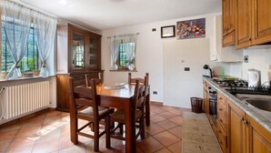 Een keuken met een eettafel, stoelen, houten kastjes, een betegelde spatwand en een raam met gordijnen.