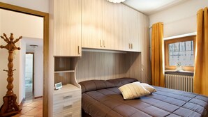 Een slaapkamer met een bed, een houten kledingkast, een tafeltje en een raam met gordijnen.