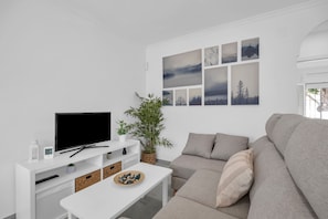 Un salon moderne avec un téléviseur à écran plat, un canapé, une table basse et un mur décoré de tableaux encadrés.