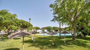 Un área de piscina con césped, árboles y sombrillas de paja.