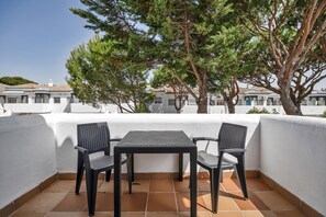 A balcony with a table and chairs, surrounded by white walls and a tree.