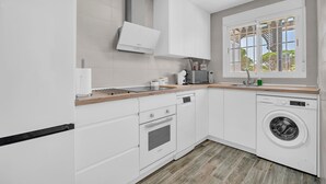 Una cocina moderna con armarios blancos, horno empotrado, lavavajillas y lavadora.