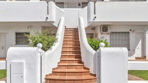 Una escalera conduce a un edificio blanco con una reja metálica y una planta pequeña en la parte superior.