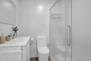 A modern bathroom with a glass shower enclosure, a white sink with a mirror, and a toilet.