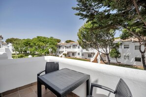 A balcony with a table and chairs, overlooking a courtyard with buildings and trees.