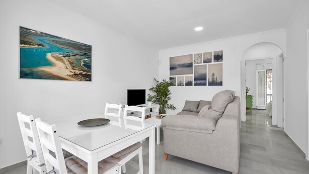 Una sala de estar moderna con comedor, un sofá gris, muebles blancos y un cuadro grande de paisaje.
