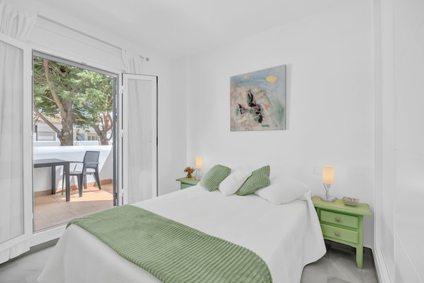 Une chambre à coucher avec un lit, une table de chevet verte, un tableau et une vue sur un patio avec une table et des chaises.