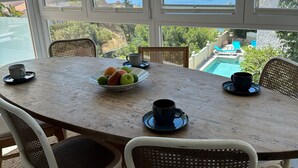 Ein Esstisch mit Stühlen, eine Schale Obst und Tassen, mit Blick auf einen Pool und den Ozean.