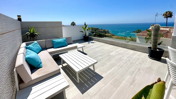 Eine Dachterrasse mit einer Couch, einem Tisch und Topfpflanzen.