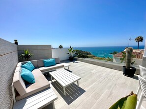 A rooftop terrace with a sofa, a table, and potted plants.