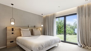 A modern bedroom with a large bed, wooden headboard, and a view of a garden through a sliding glass door. - Villa 'Belenos Piscine Vue Mer' with Sea View, Wi-Fi, and Air Conditioning (Roquebrune-sur-Argens)