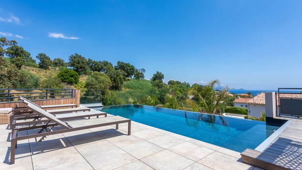 A swimming pool with a wooden deck and lounge chairs, surrounded by greenery and a view of the sea. - Villa 'Belenos Piscine Vue Mer' with Sea View, Wi-Fi, and Air Conditioning (Roquebrune-sur-Argens)