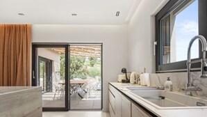 A modern kitchen with a large window, a sliding glass door leading to an outdoor dining area, and a built-in sink. - Villa 'Belenos Piscine Vue Mer' with Sea View, Wi-Fi, and Air Conditioning (Roquebrune-sur-Argens)
