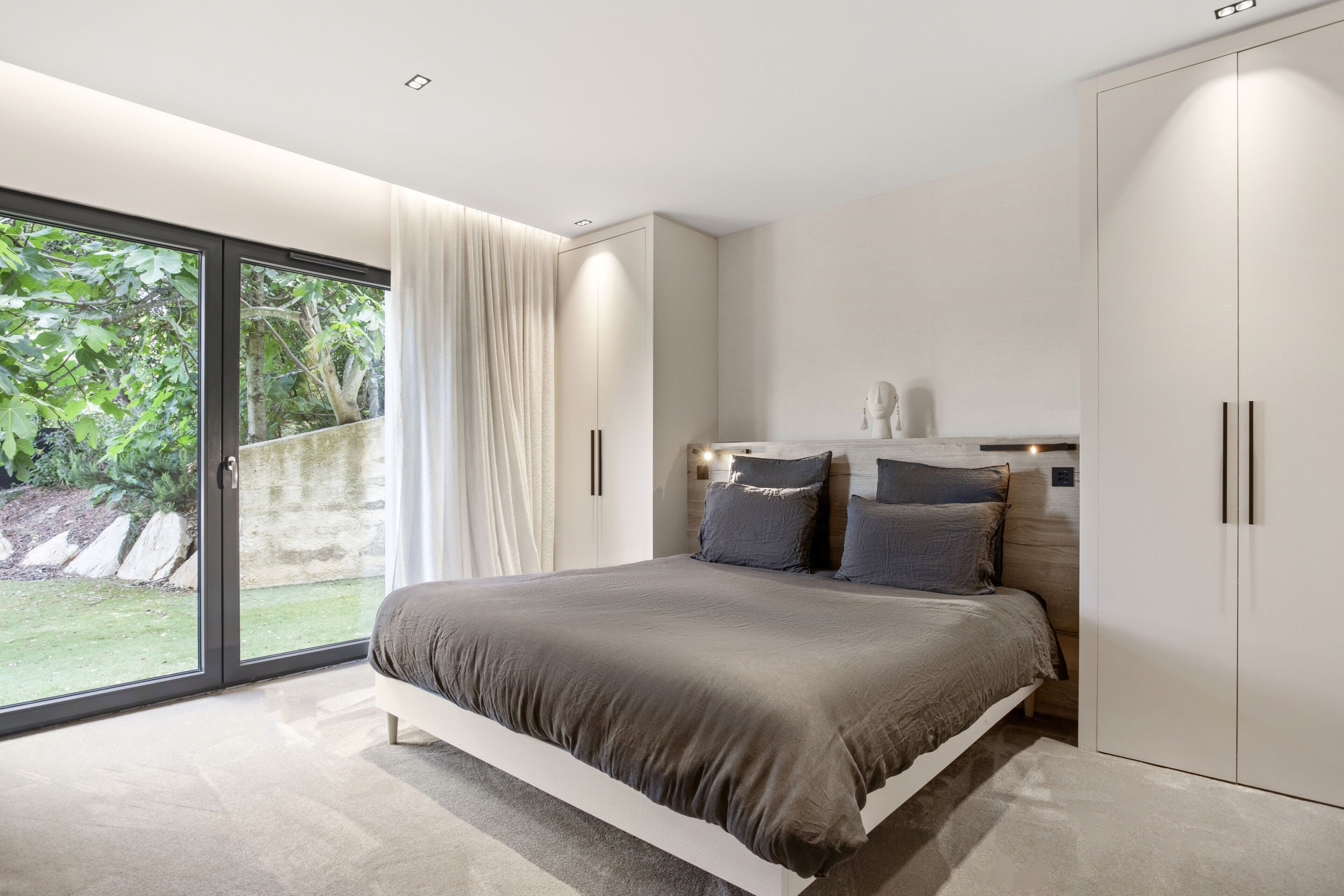 A modern bedroom with a large bed, sliding glass doors to a garden, and built-in wardrobe.