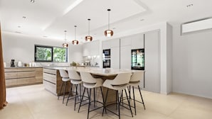A modern kitchen with a central island, bar stools, pendant lighting, and a large window. - Villa 'Belenos Piscine Vue Mer' with Sea View, Wi-Fi, and Air Conditioning (Roquebrune-sur-Argens)