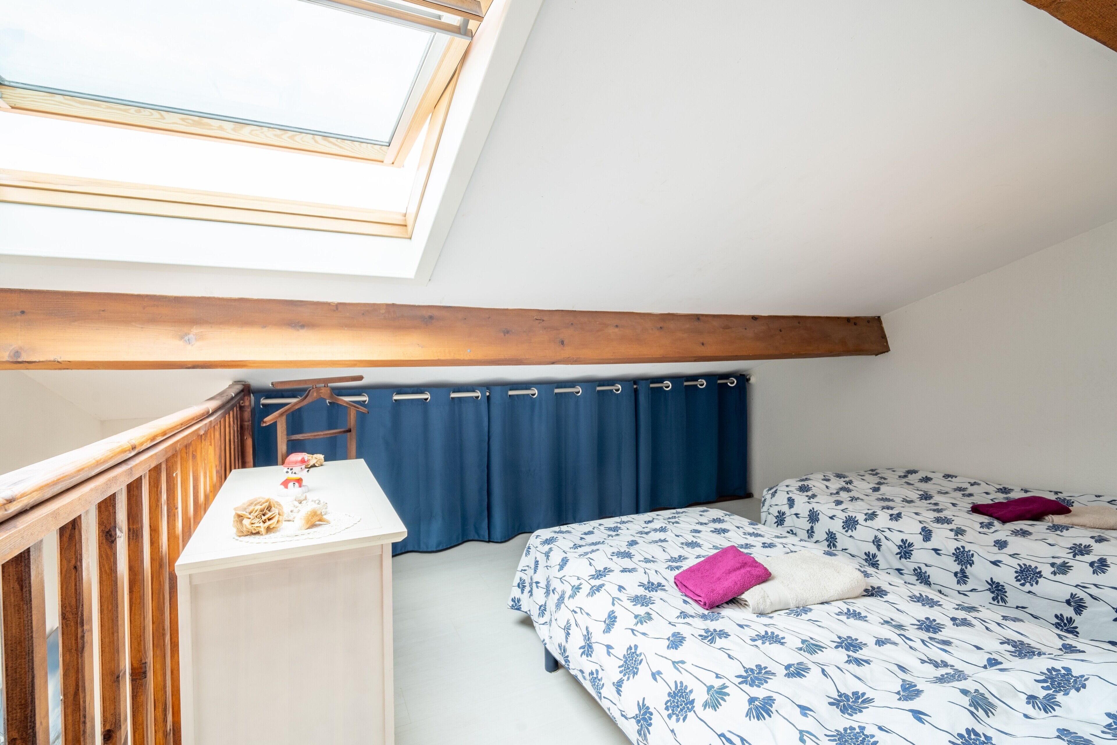 Un dormitorio con tragaluz, cama con ropa de cama floral, mesita de noche con lámpara y cabecera de madera.