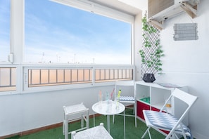 Une pièce avec une grande fenêtre, une petite table avec des chaises, une étagère blanche et une plante fixée au mur.