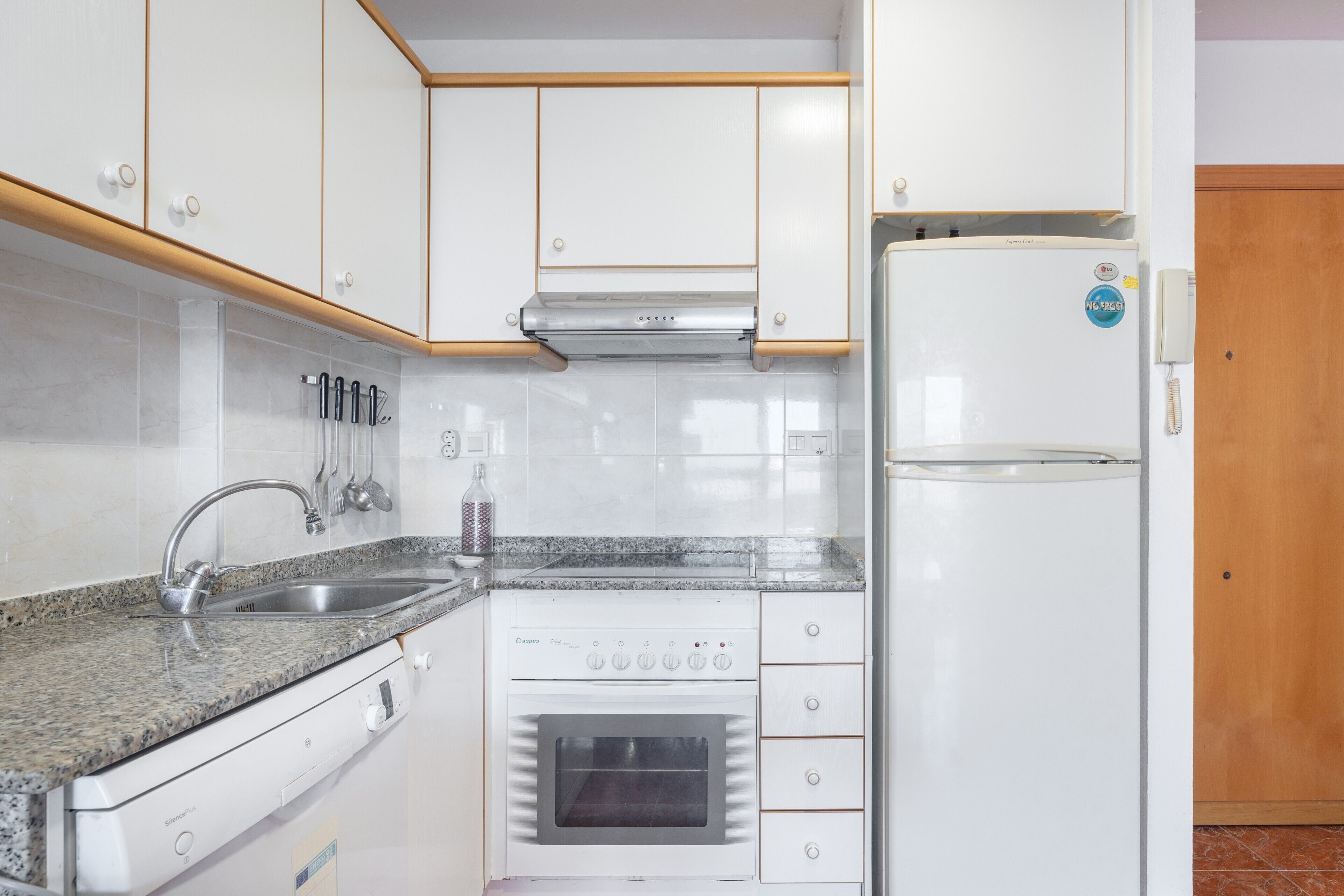 Una cucina compatta con mobili bianchi, un lavello in acciaio inossidabile, forno integrato e frigorifero.