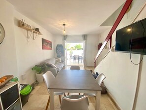 Ein Essbereich mit Tisch und Stühlen, einer Couch, einem an der Wand befestigten Fernseher und einer Treppe.