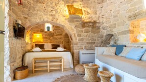 Una habitación con paredes de piedra, una cama, un sofá, una mesita y un banco.