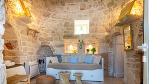 Habitación con paredes de piedra, una cama, una mesita y un banco.
