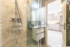 A modern bathroom with a glass shower enclosure, a vanity with a mirror, and a kitchen visible through an open door. - Apartment 'Sea View Paradize' with Sea View, Wi-Fi and Air Conditioning (Fuengirola)