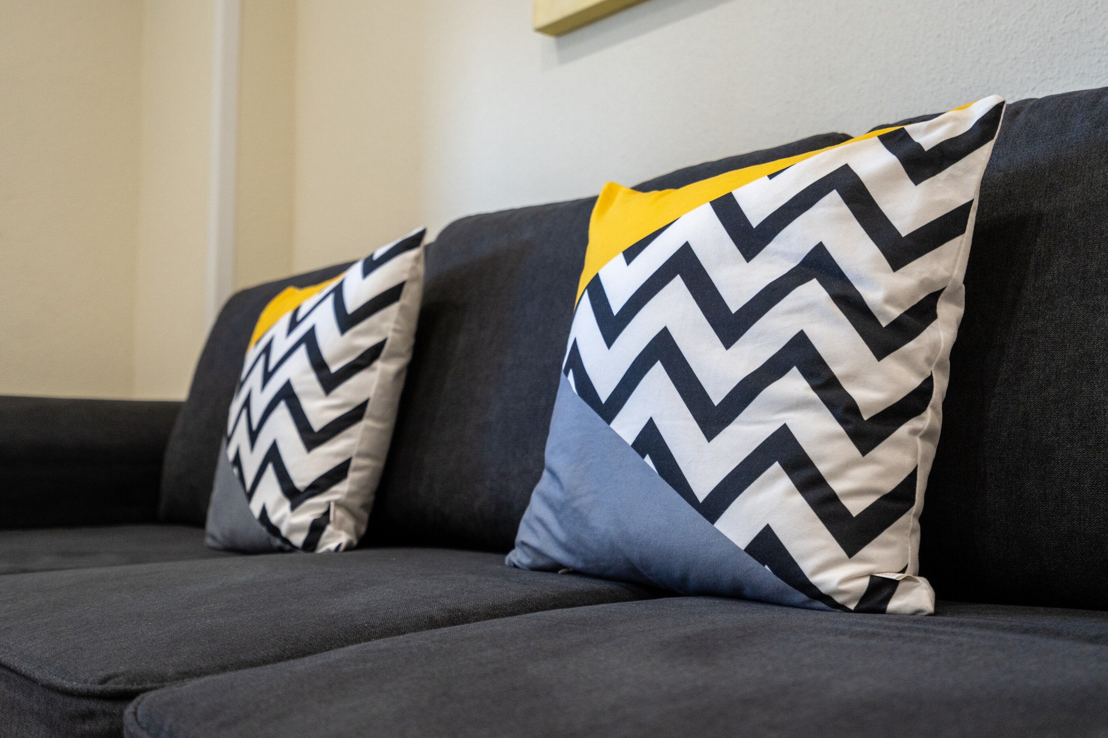 A dark-colored sofa with two patterned pillows, one with a zigzag design and another with a yellow top.