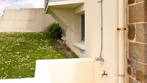 A building with a stone facade, a blue window, and a small garden with white flowers.